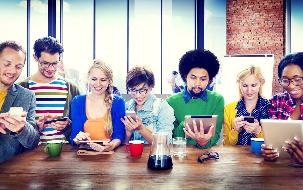 Grupo diverso de personas alrededor de una mesa usando smartphones y tablets, que simboliza la formación online para peluqueros y barberos